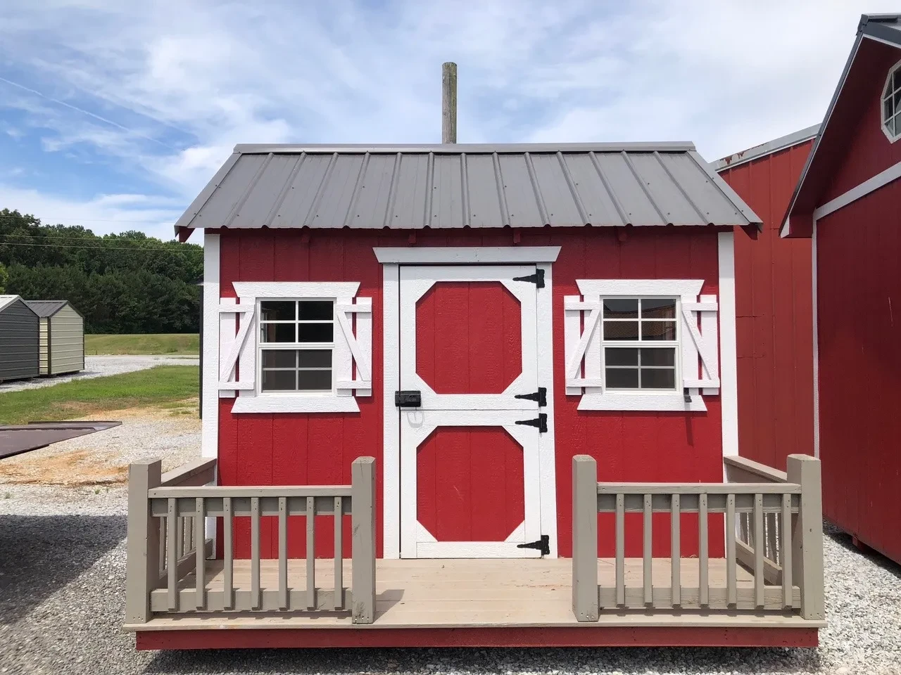 a red playhouse with white trim and a charcoal colored metal roof. It also has a small porch