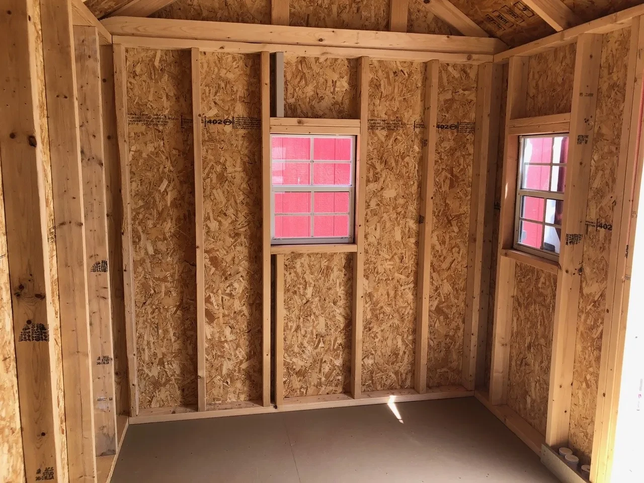 inside a wood playhouse looking at the right wall. It shows a window in it and you can see another window on the front wall