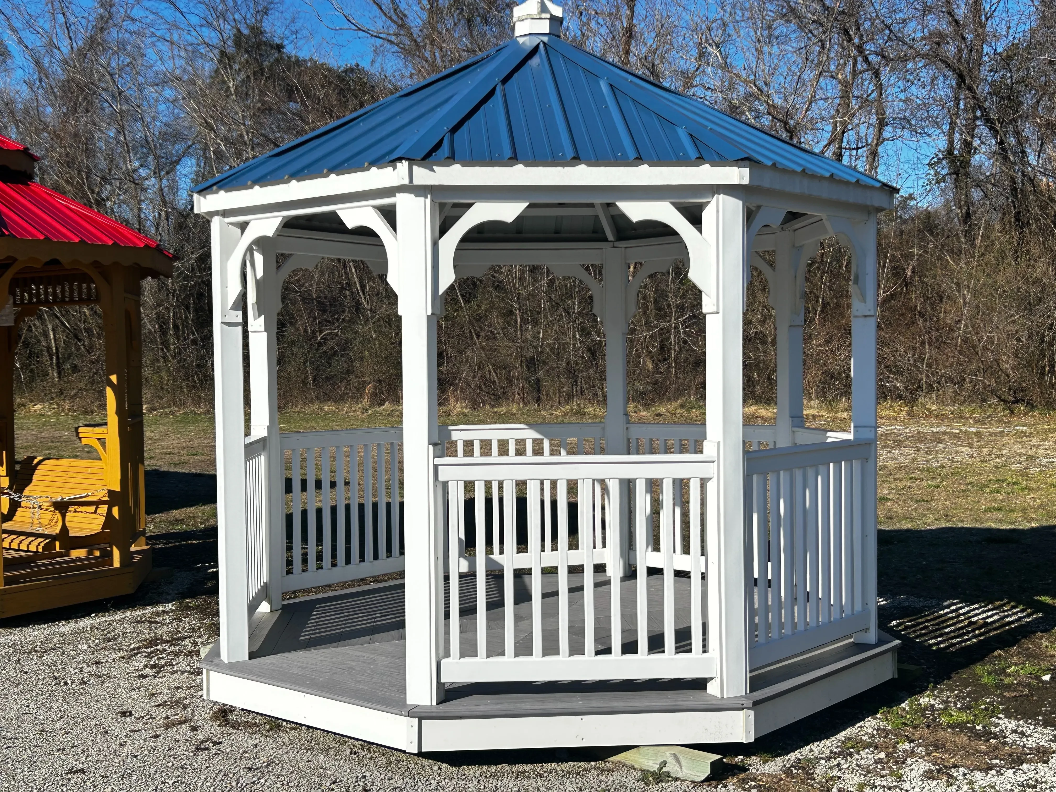 a white gazebo with posts and railings. It also has a blue metal roof