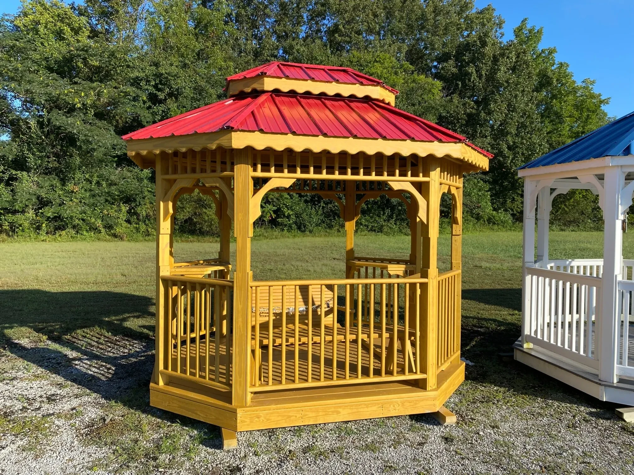 a wood stained teahouse and a red metal roof, it has benches inside.