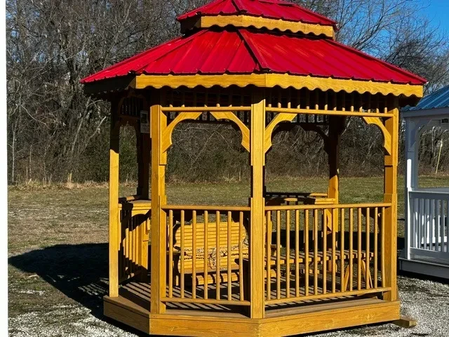 a wood teahouse stained a honey gold color, it has benches inside and a red metal roof
