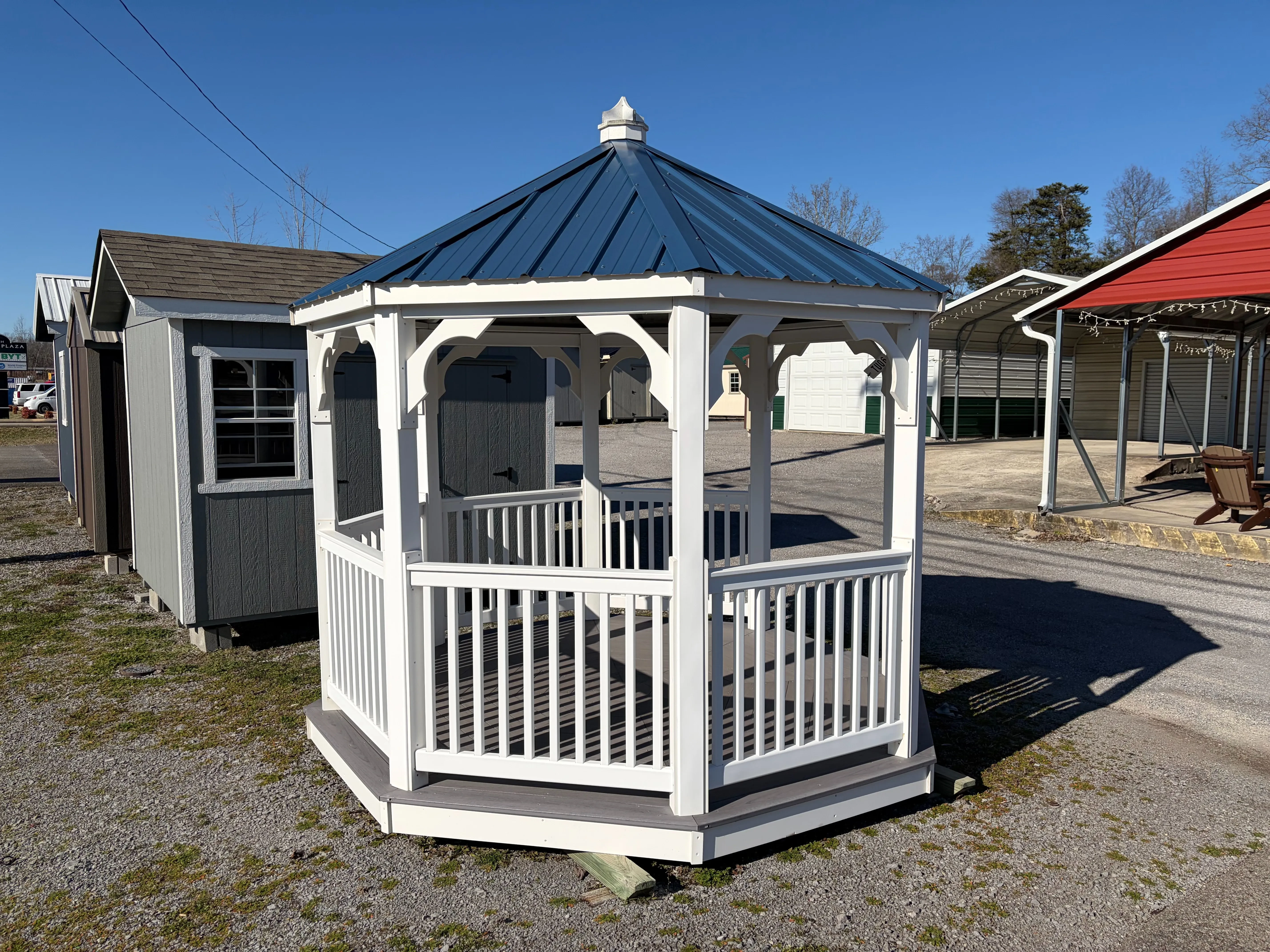 a white vinyl gazebo with white posts and white railings. It has decorative trim and a blue metal roof