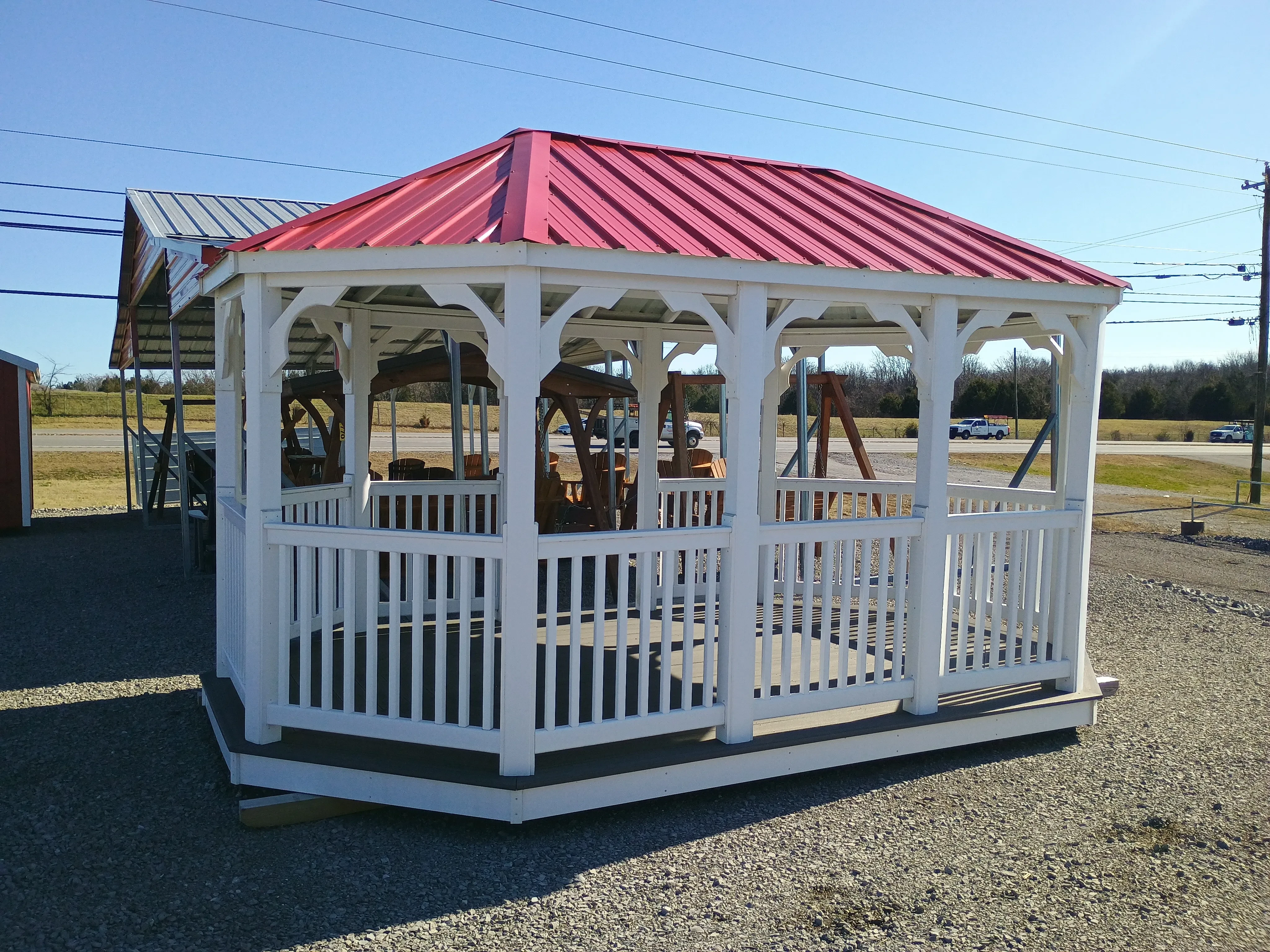 a large white vinyl gazebo with white posts and railings, it also has a bright red metal roof