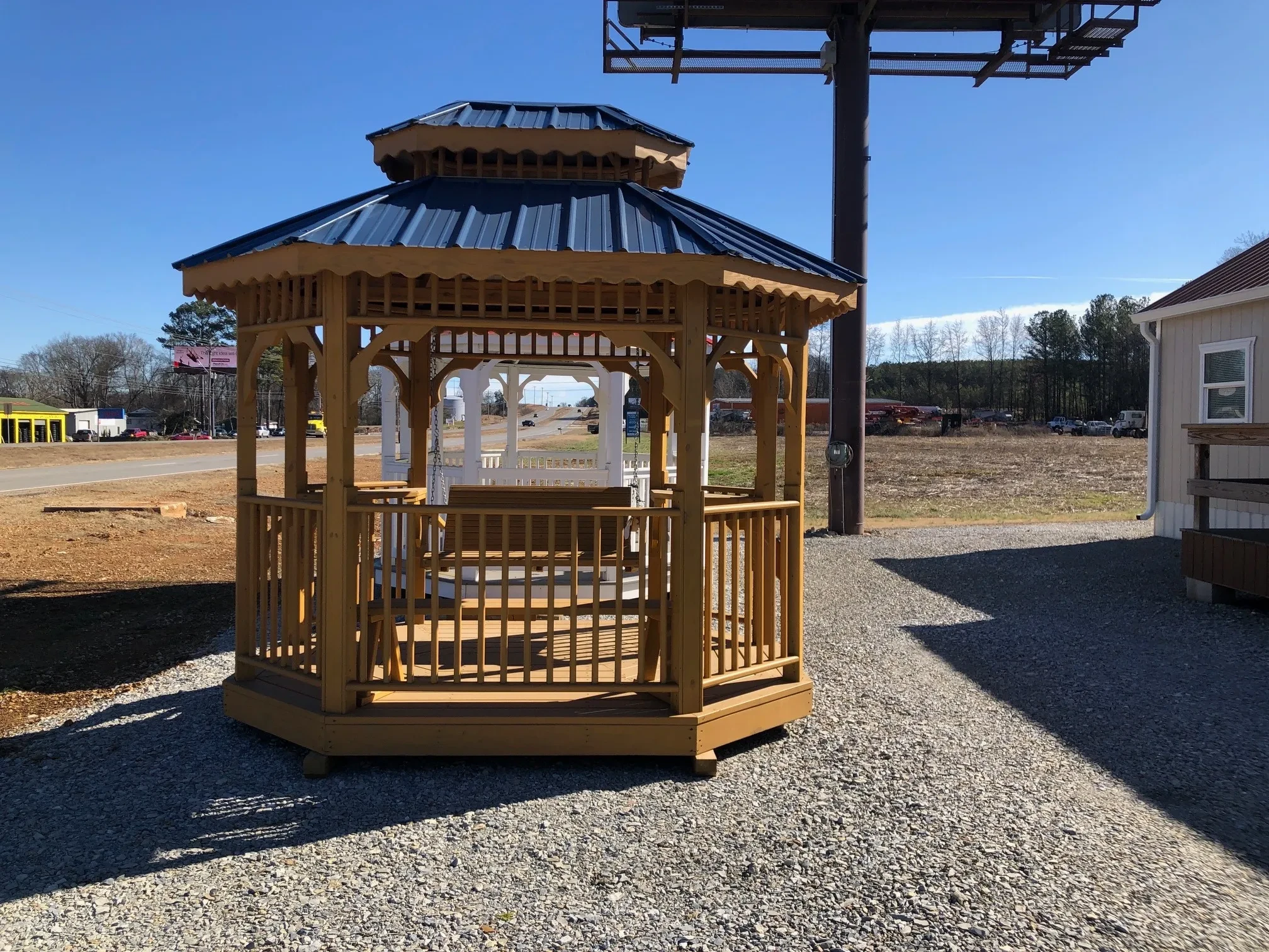 a honey gold stained teahouse with an opening to walk through, and a bench inside. It also has a double roof with blue metal