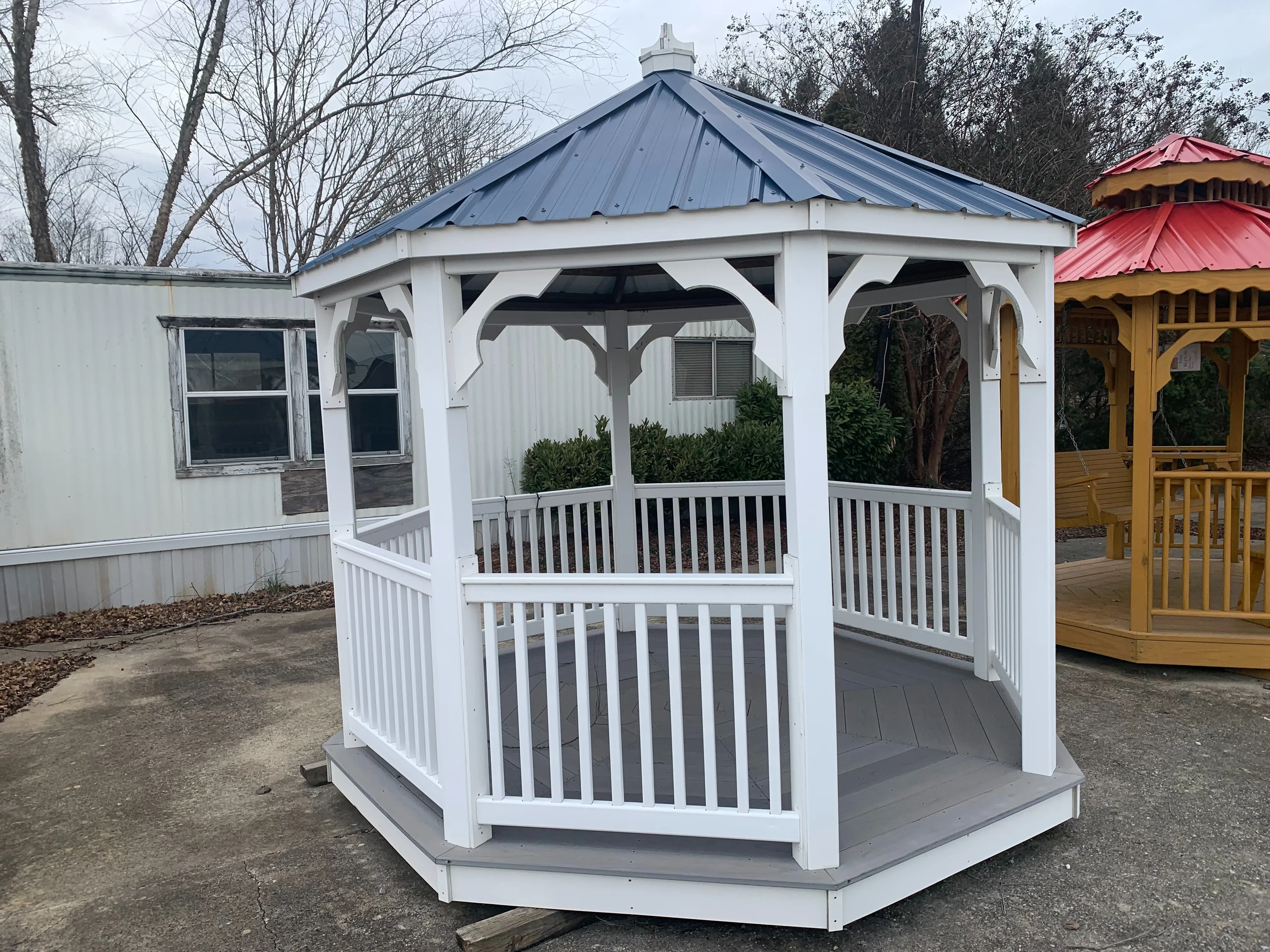 a white gazebo with white posts and rails. It has a single blue metal roof
