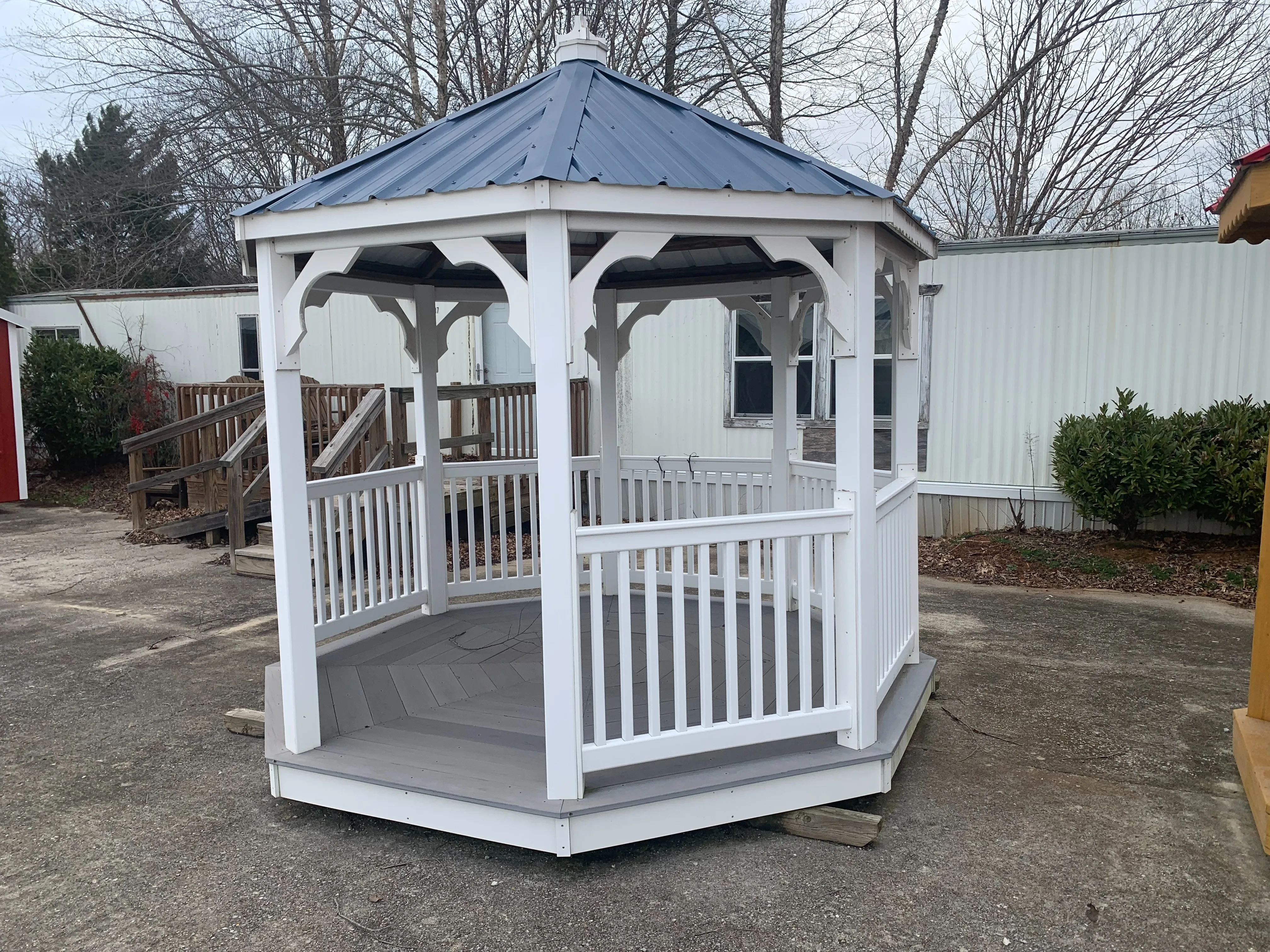 a white gazebo with a blue metal roof. It has an opening to walk through and gray vinyl flooring