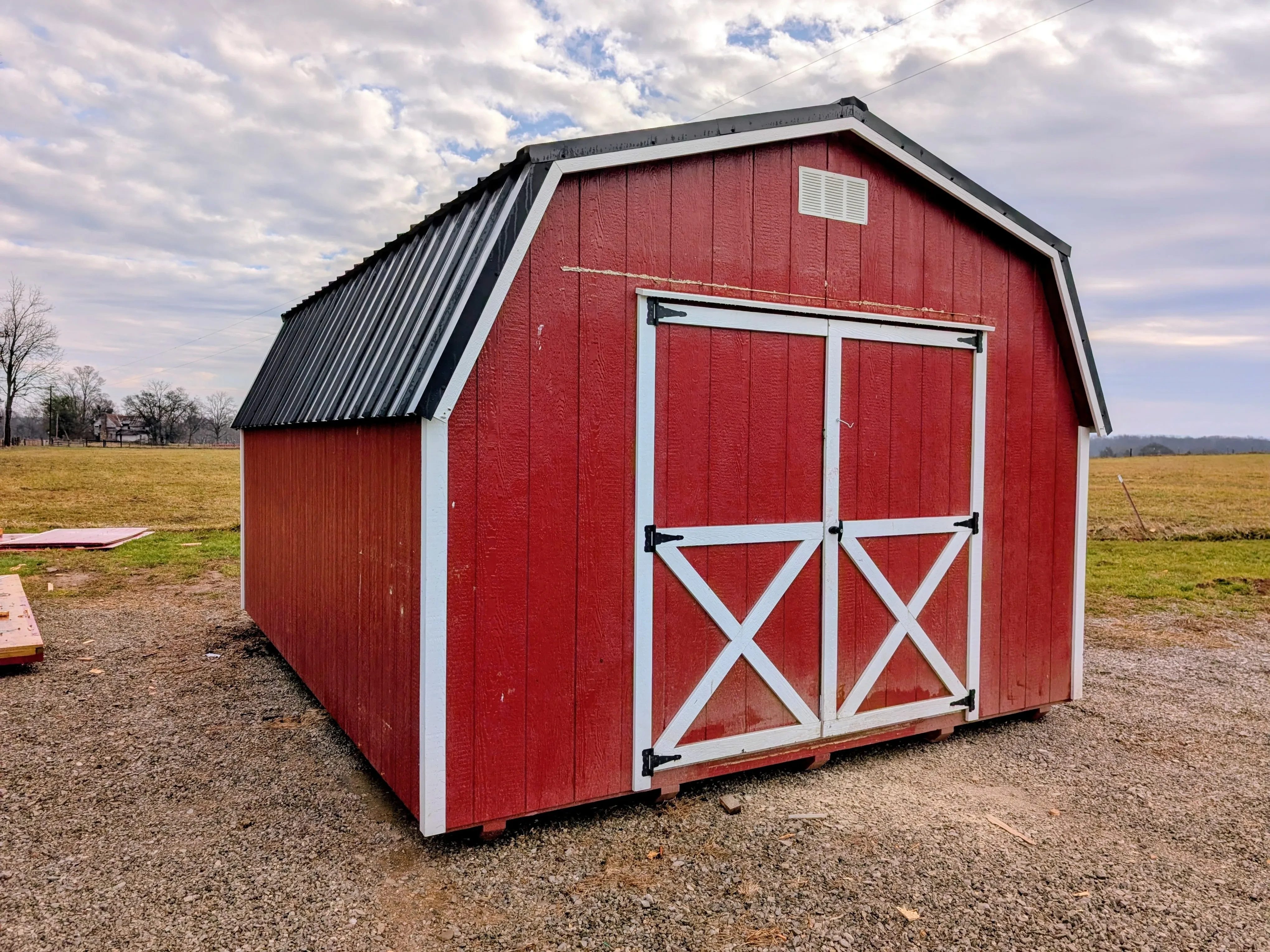 a red dutch style barn with white trim and a black metal roof. It has a vent in the front towards the roof