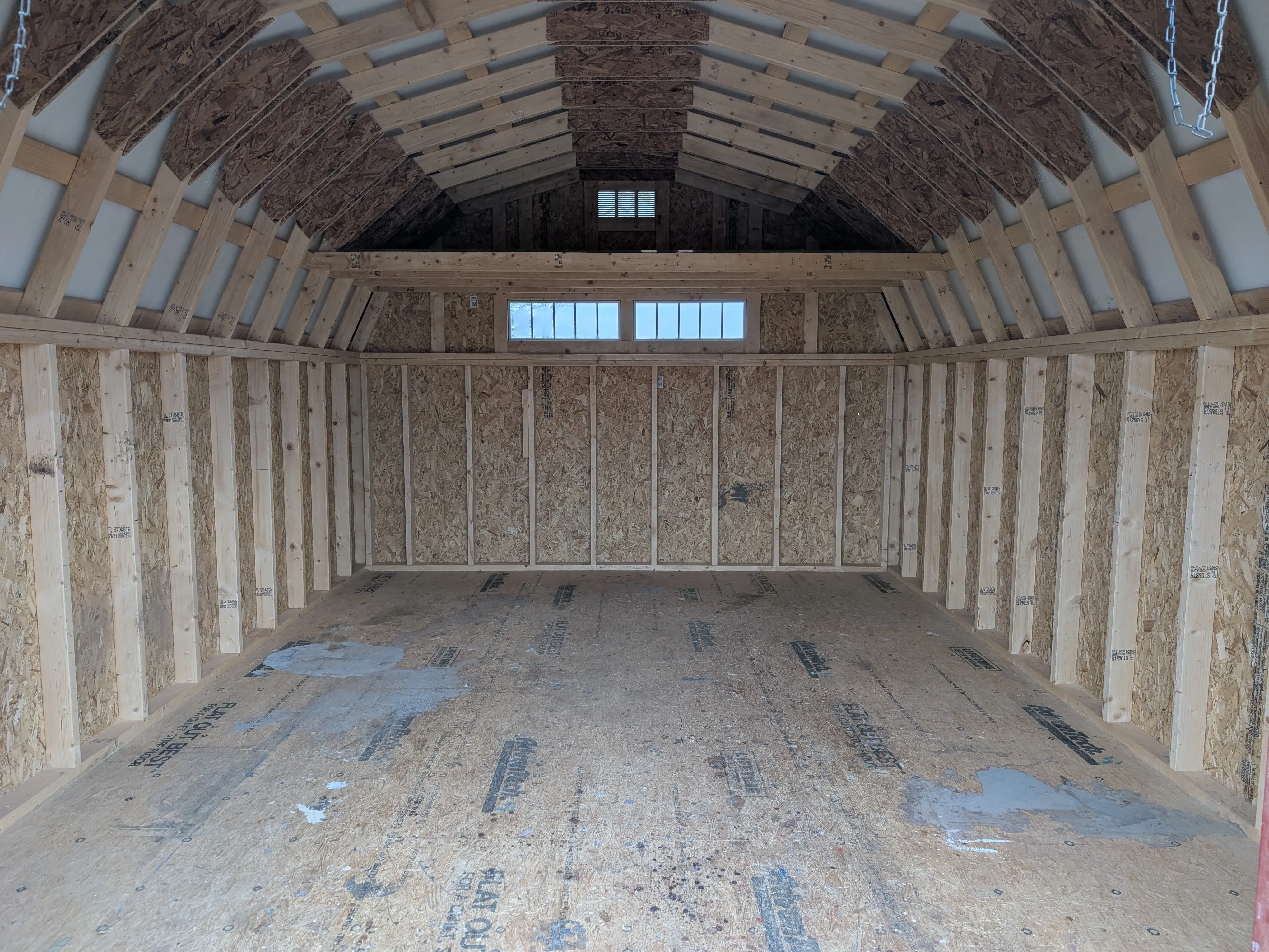 inside a wood lofted barn looking towards the back wall. There are two transom windows on the back wall and a loft