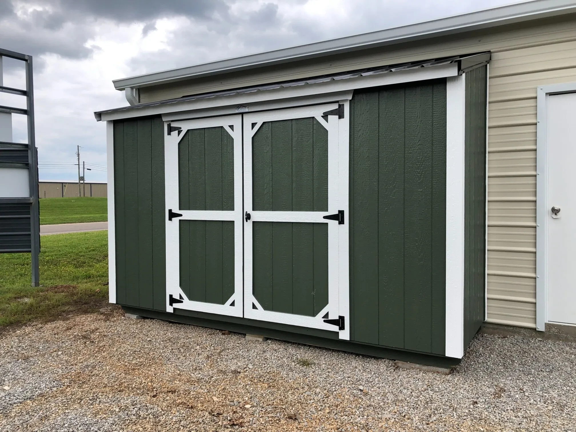A green lean-to style shed against a garage.