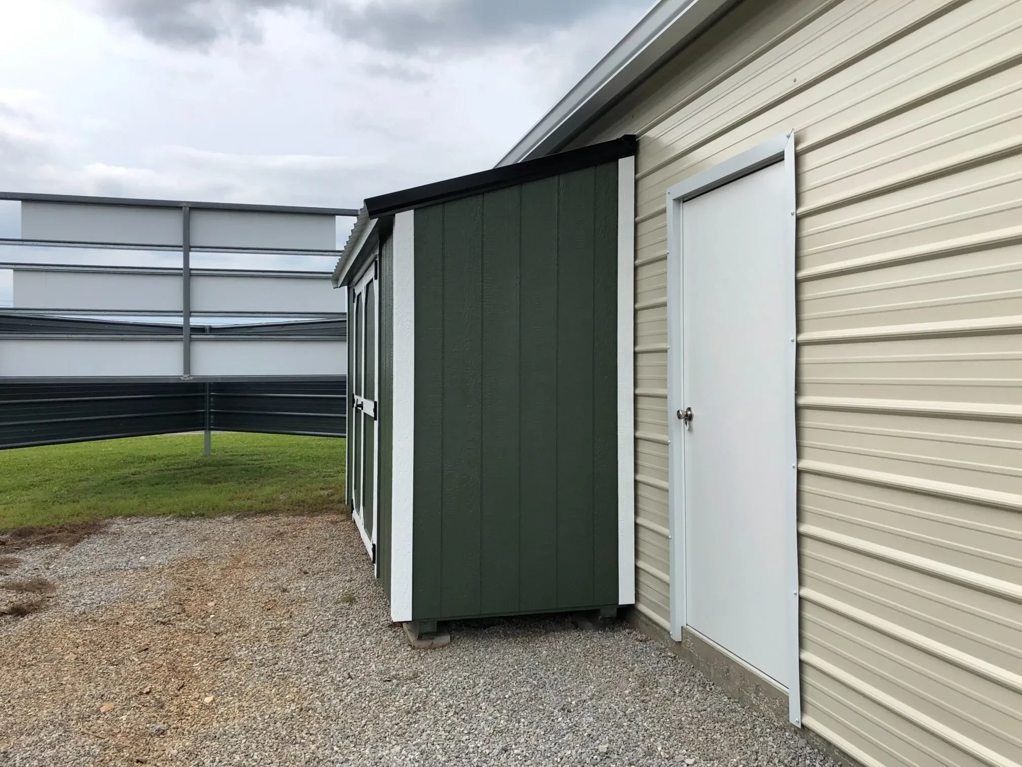 Side view of a green lean-to style shed up against a garage.